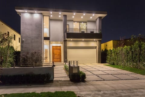 Two-story modern home with a wood front door, lit at dusk, with a paved front drive