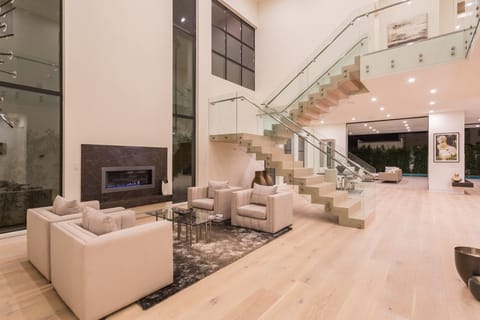Inside the same home, a bright double-height living room with a floating staircase and glass railings